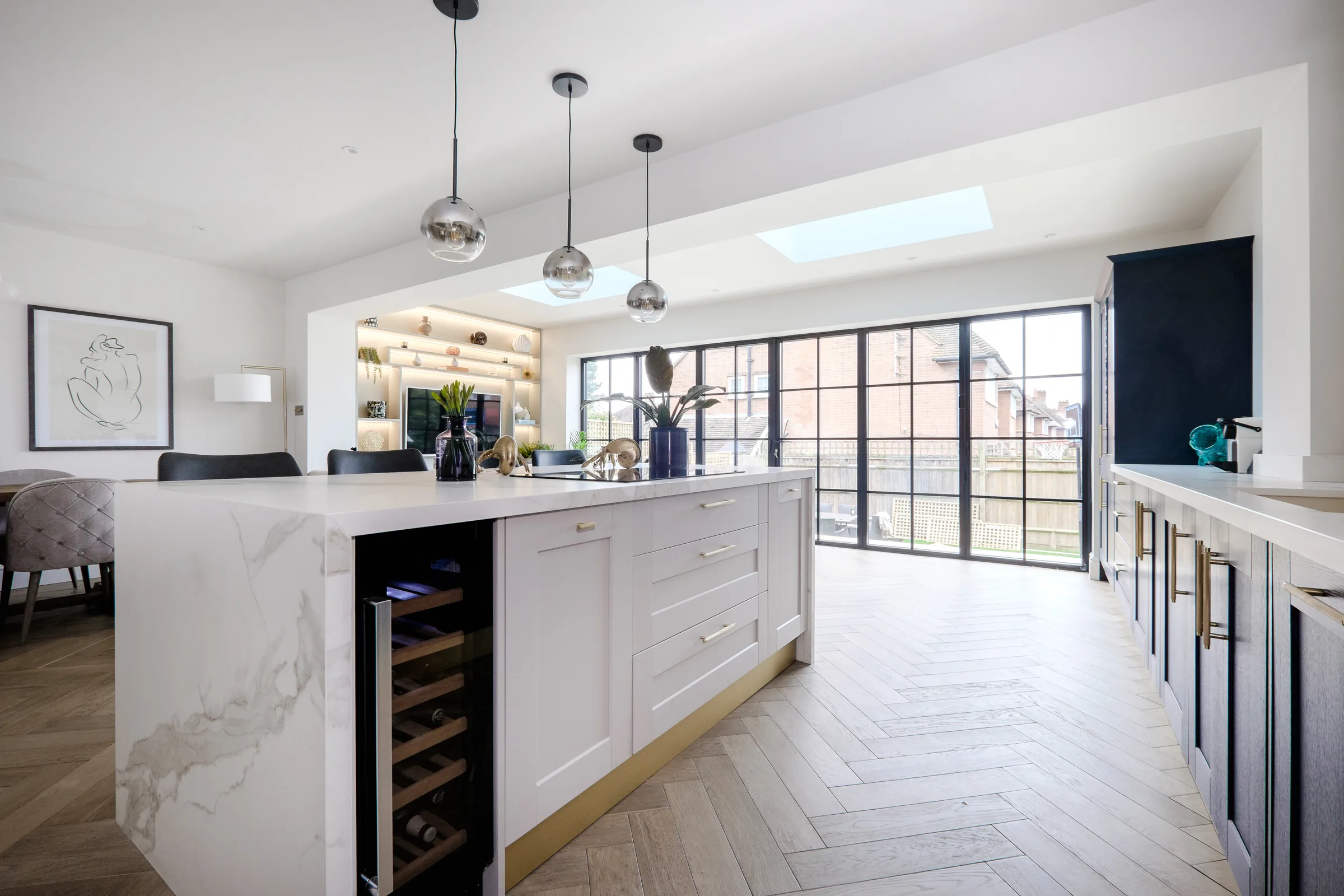 Open-plan kitchen extension with a marble waterfall island, herringbone oak floor, rooflights and black-framed glazed doors to the garden