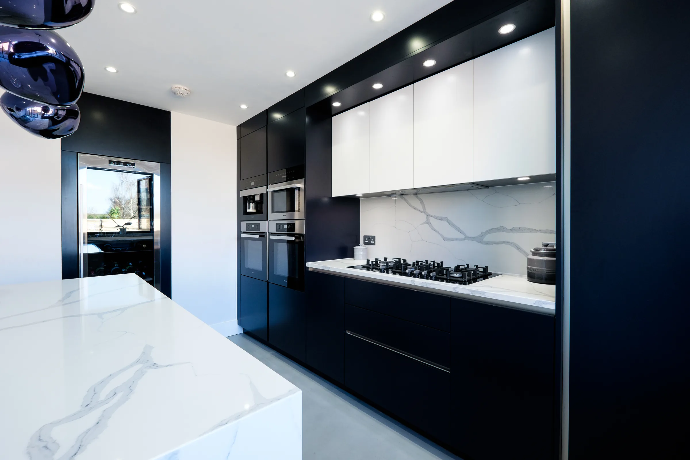 Contemporary kitchen with dark cabinetry, a marble splashback and a marble-topped island