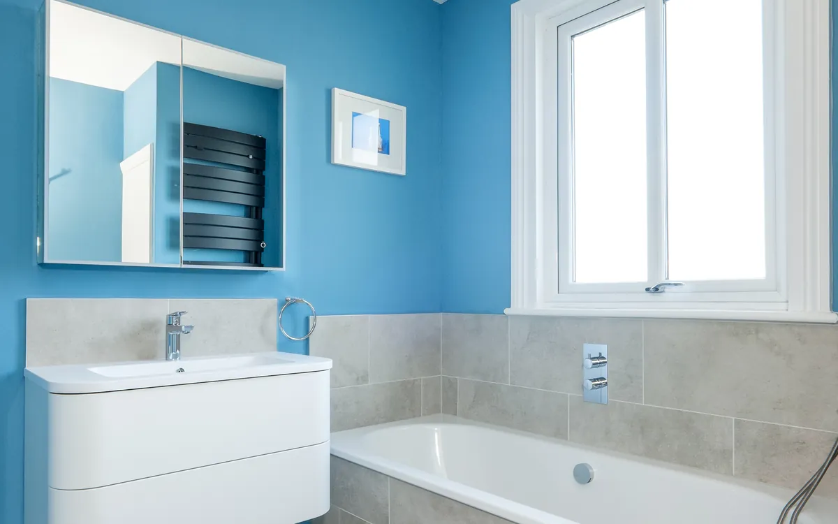 Family bathroom with a white wall-hung vanity, mirrored cabinet, stone-effect tiling and a built-in bath