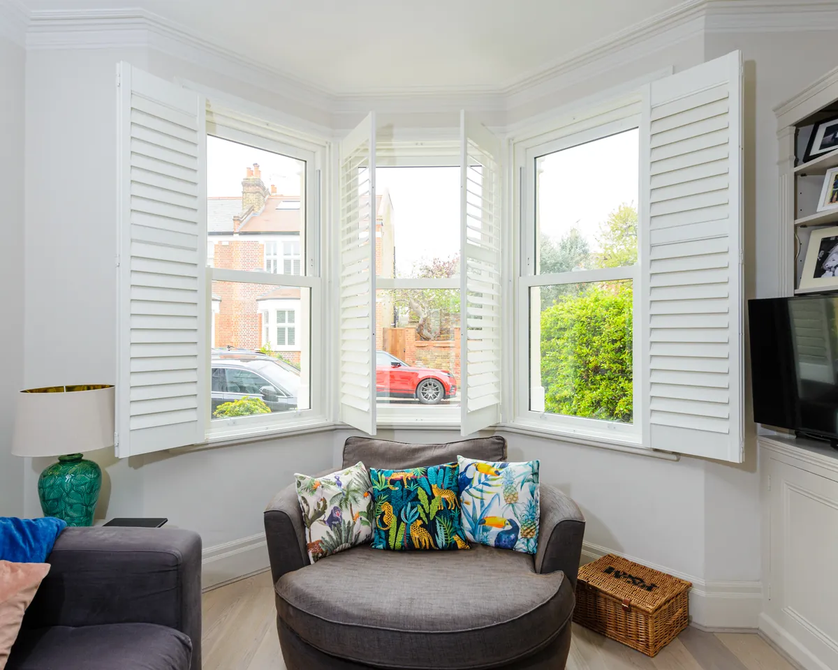 Bay window snug with white shutters and a round armchair with colourful cushions