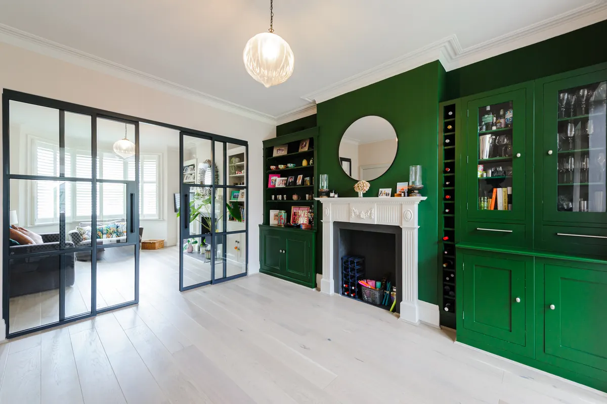 Period living room with deep green built-in joinery, a white marble fireplace and steel-framed glass doors