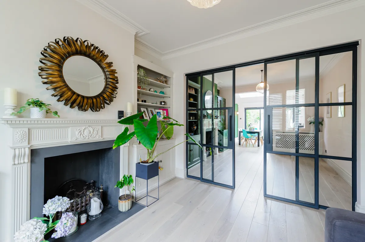 Period living room with a white marble fireplace and sunburst mirror, opening through steel-framed glass doors