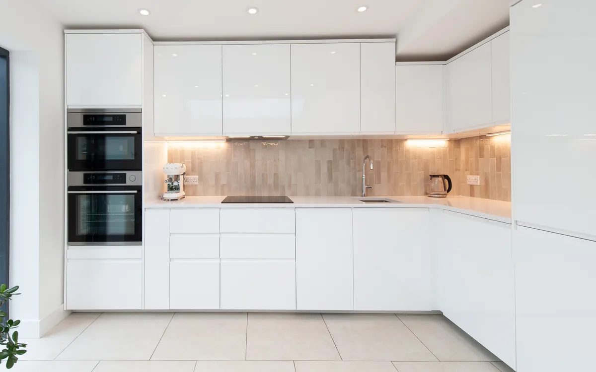 Bright white gloss kitchen with a textured tile splashback and full-height glazing onto the garden
