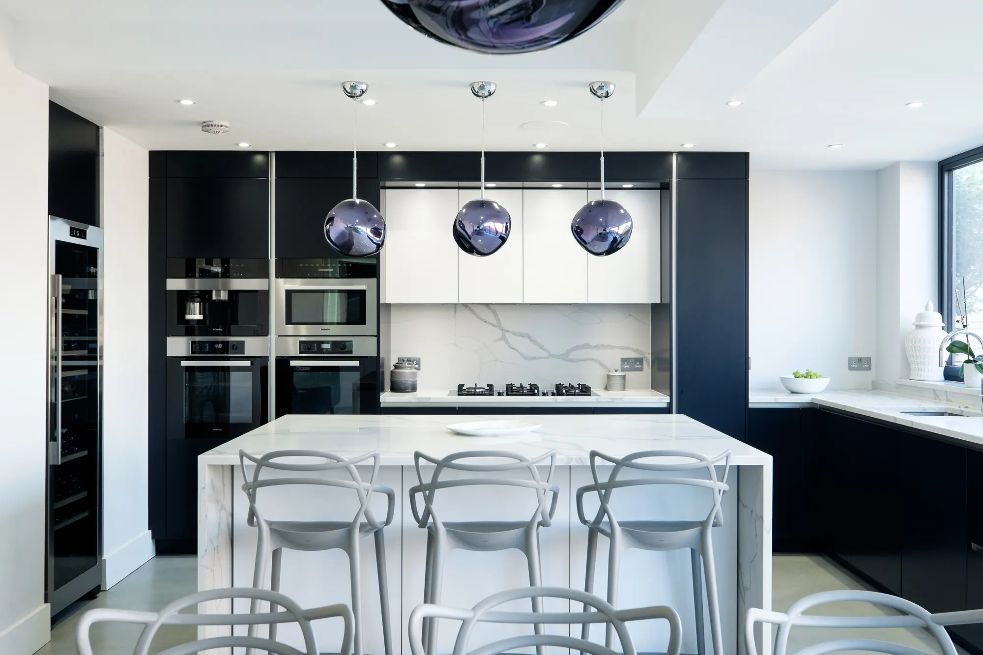 Contemporary kitchen with dark handleless cabinetry, a marble-effect splashback and island, and three smoky glass pendants