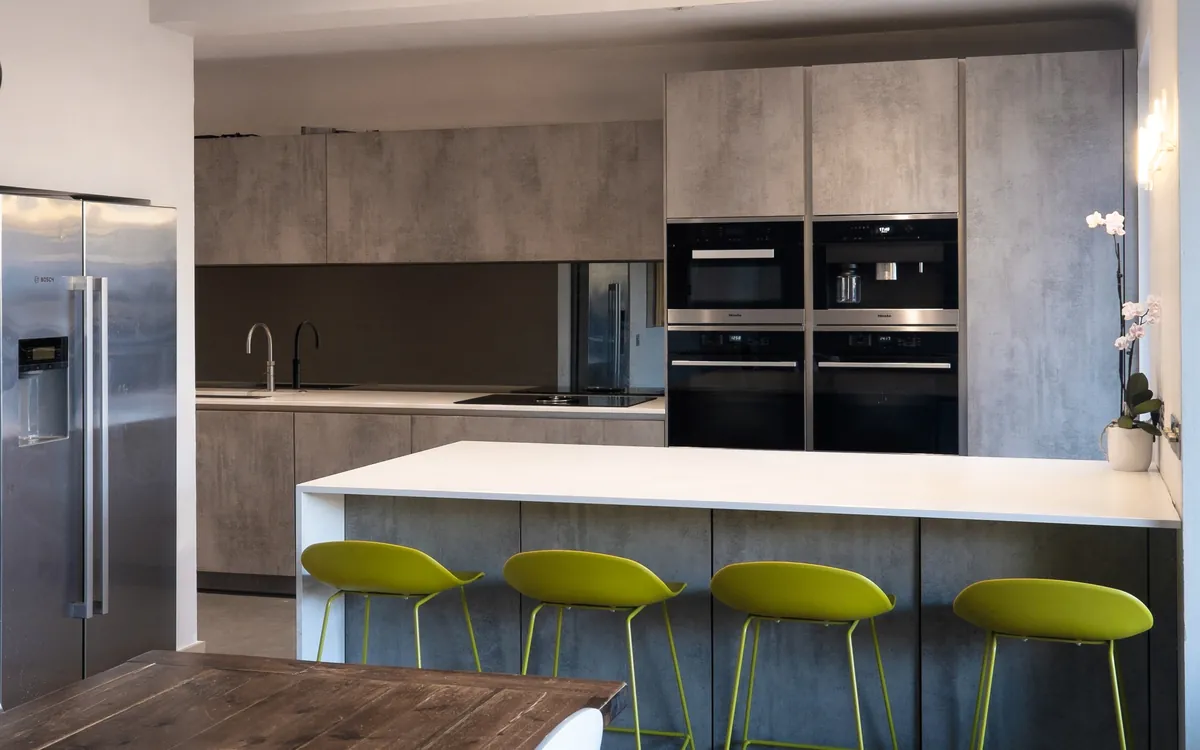 Concrete-effect kitchen with a white island, lime green bar stools and a walnut dining table