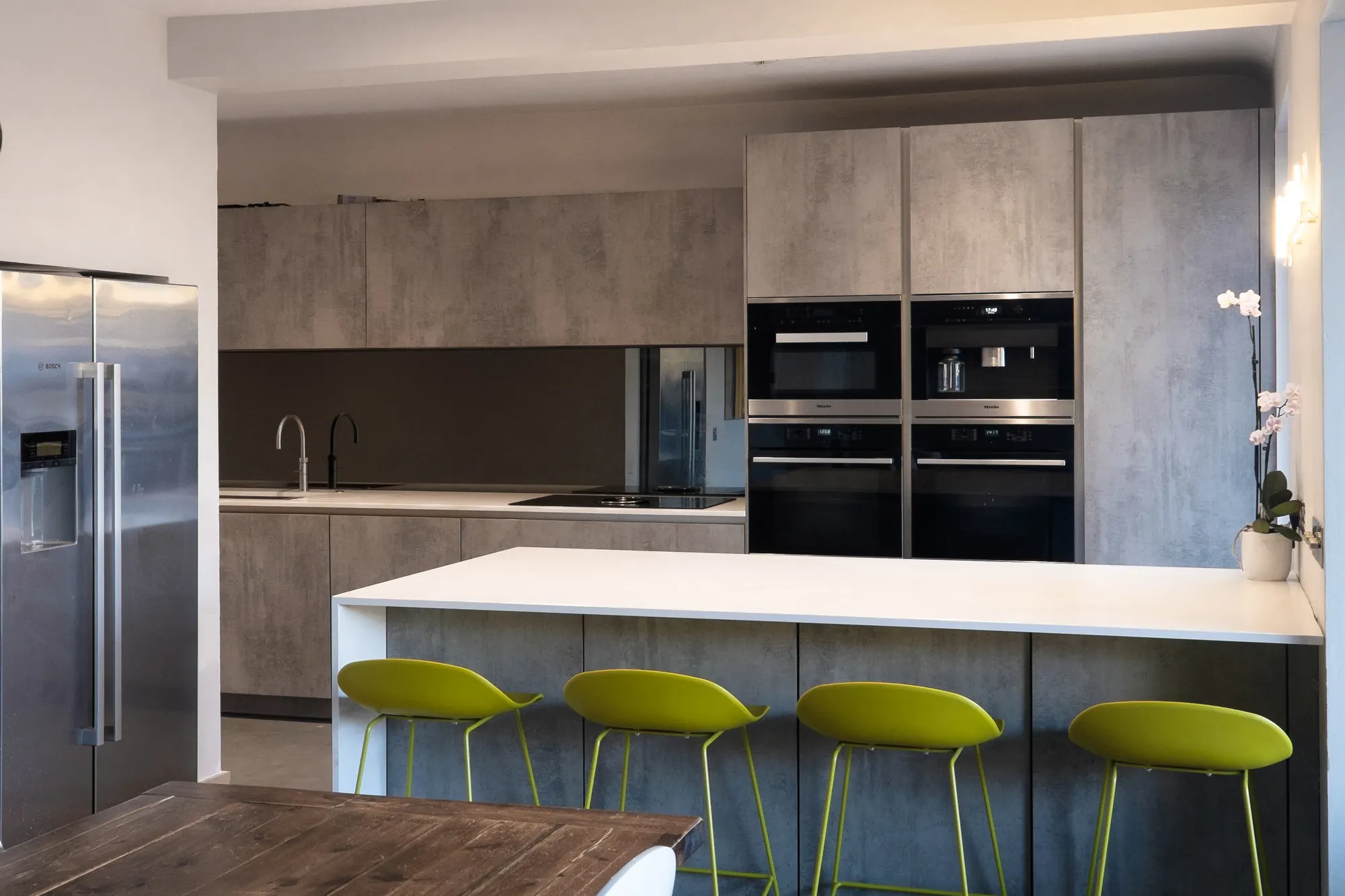 Open-plan kitchen with concrete-effect cabinetry, a white island with lime green bar stools and a walnut dining table