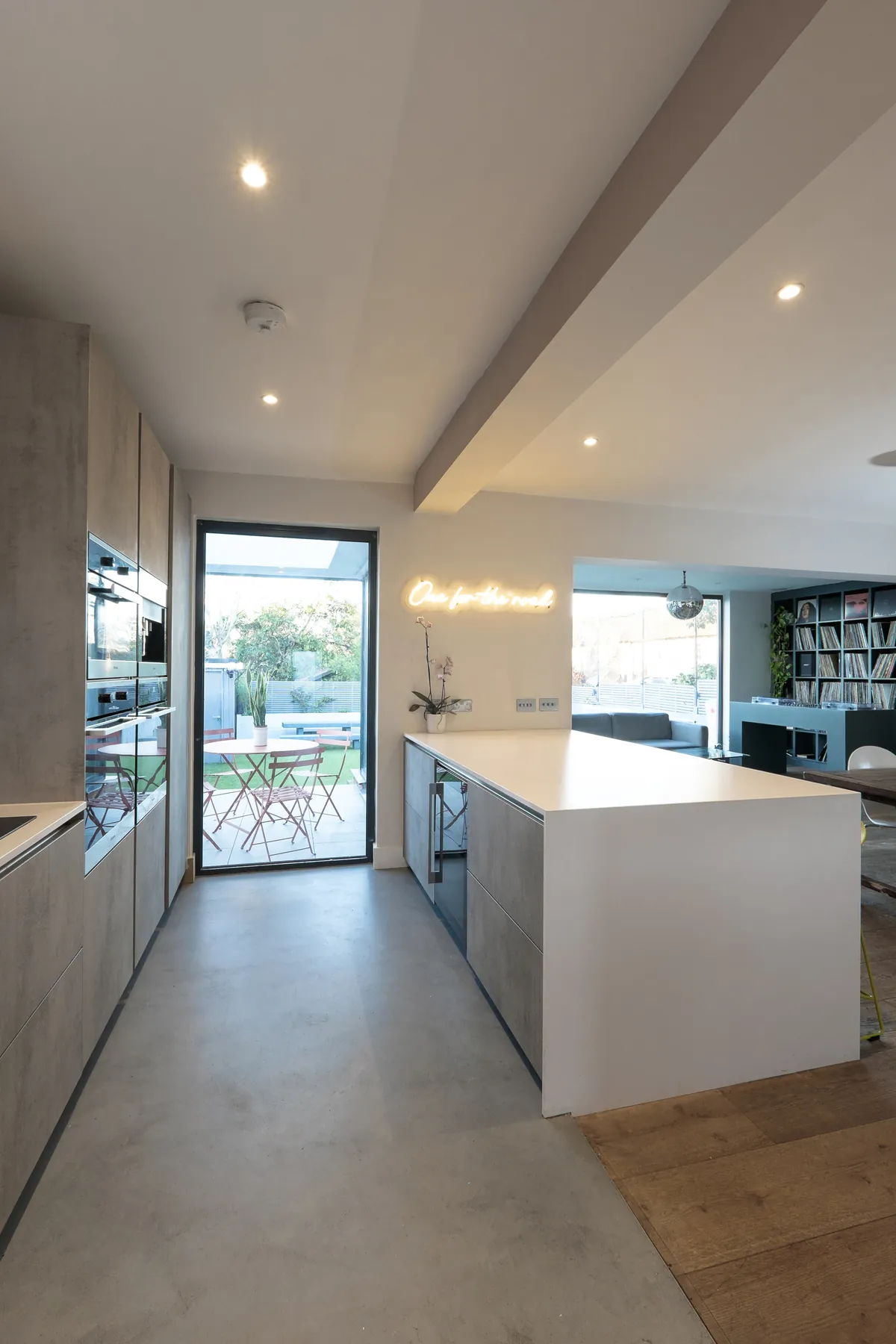 Kitchen with concrete-effect units and a white island, looking through a glazed door to the garden
