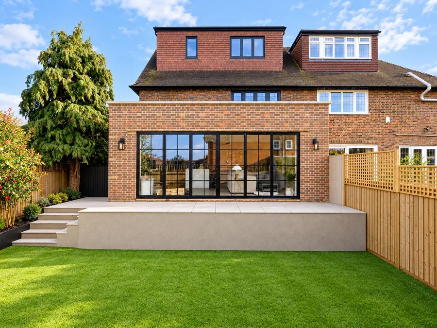 Brick rear extension with full-width black-framed glazing, seen across the garden lawn