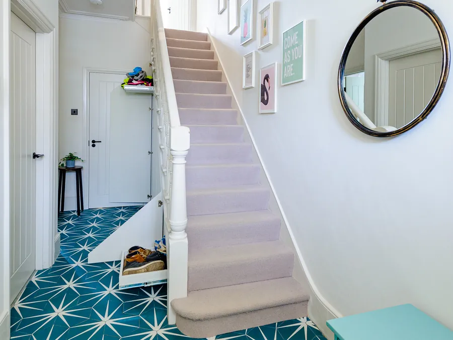 Hallway with teal star-pattern floor tiles leading to a carpeted staircase and a round mirror