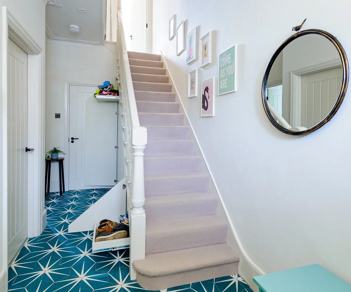 Hallway with teal star-pattern floor tiles leading to a carpeted staircase and a round mirror
