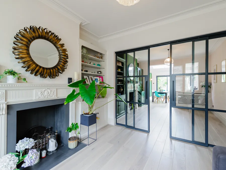 Period living room with a marble fireplace and sunburst mirror, opening through steel-framed glass doors